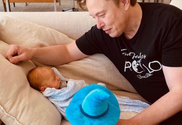 Elon Musk looking at a new baby on an off-white couch.