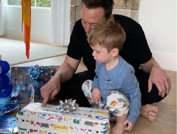 Elon Musk with one of his children, looking at a present wrapped in vehicle wrapping paper.