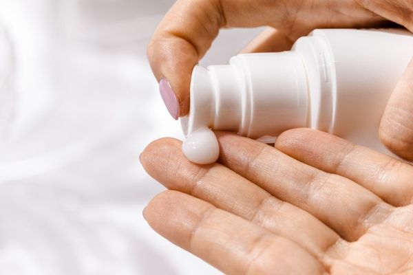 A hand pumping lotion onto another hand. White background.