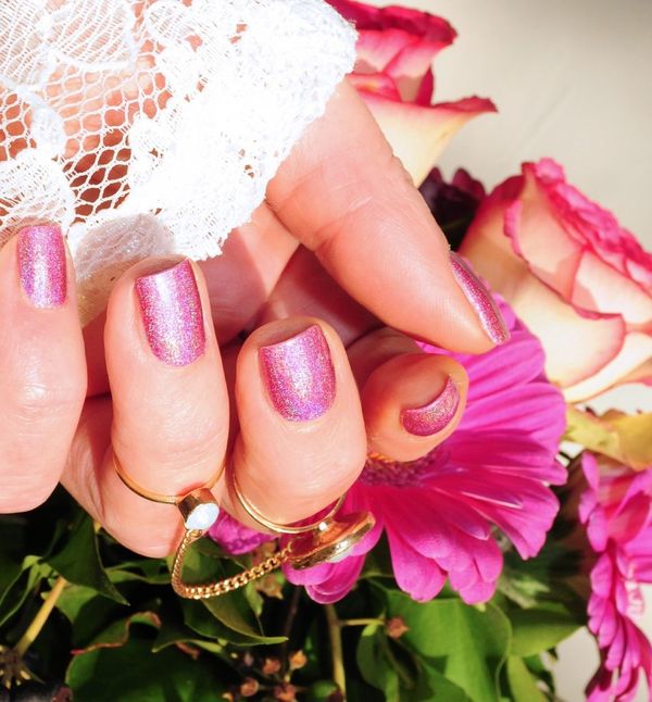 A hand with a fresh pink manicure and flowers.